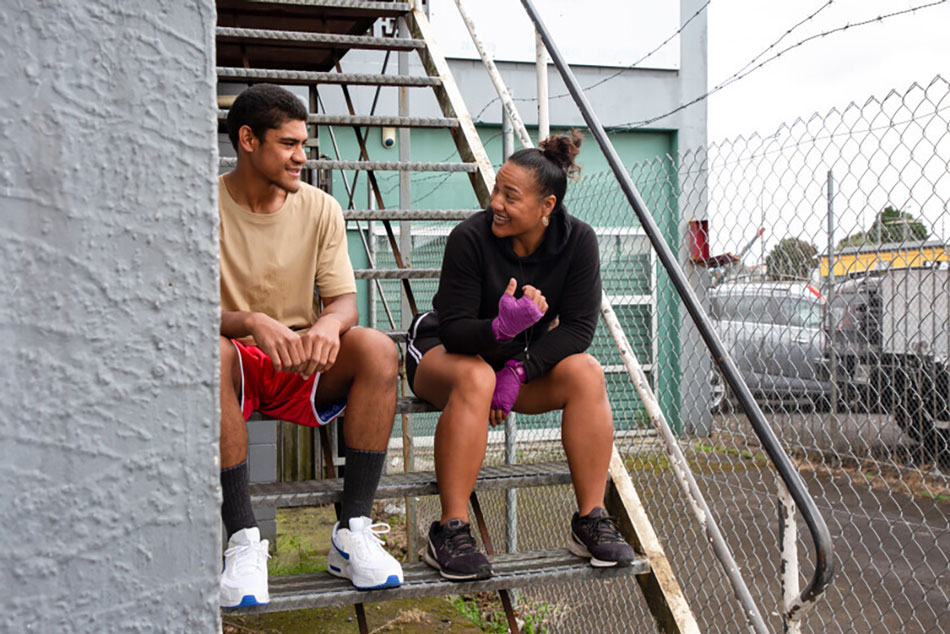 Photo of a Māori couple chatting to each other, sitting on an outdoor staircase